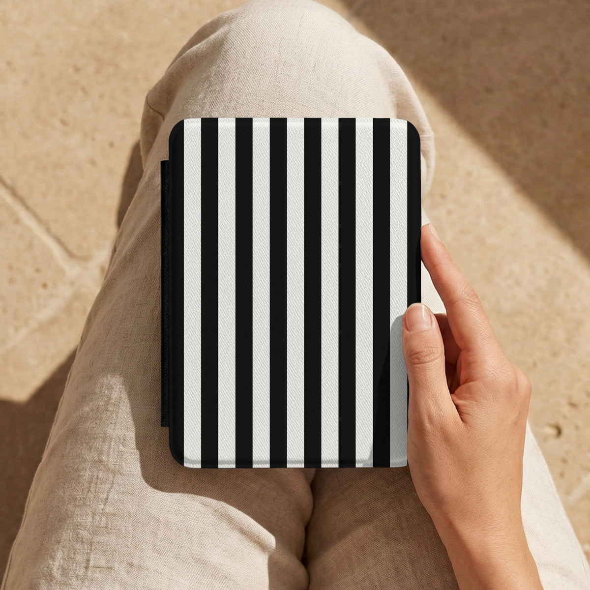 Hand holding the Black Cabana Stripe Kindle case on a lap
