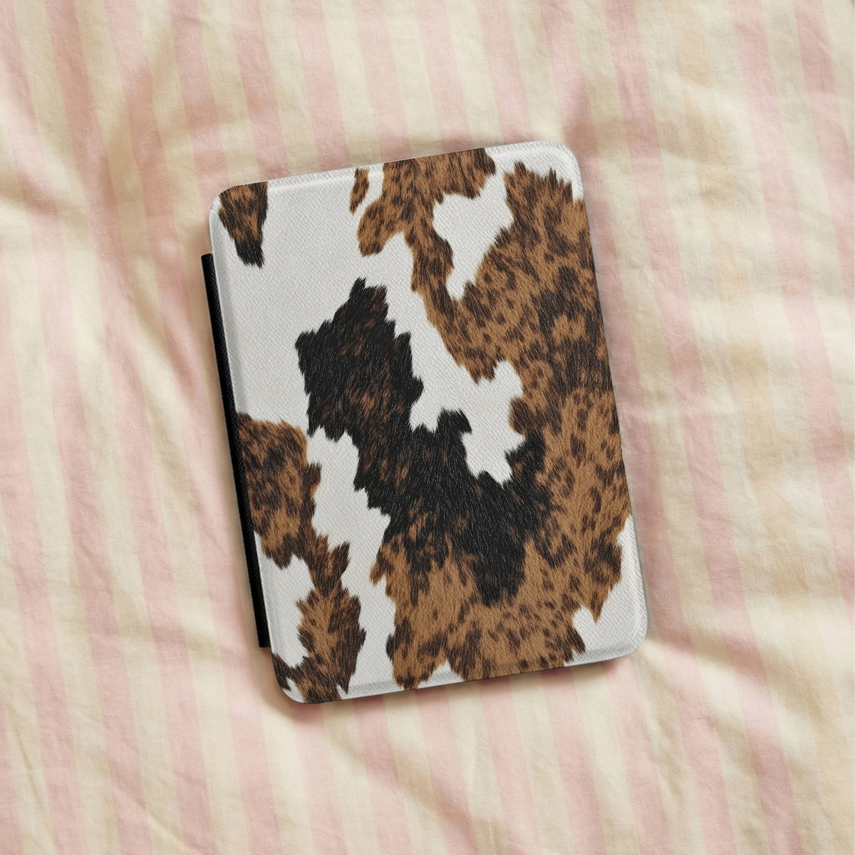 Brown Cow Print Kindle case lying on striped bedding
