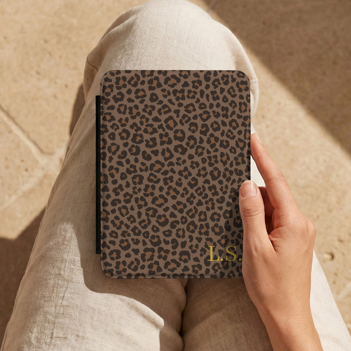 Hand holding a brown leopard print Kindle case on a lap