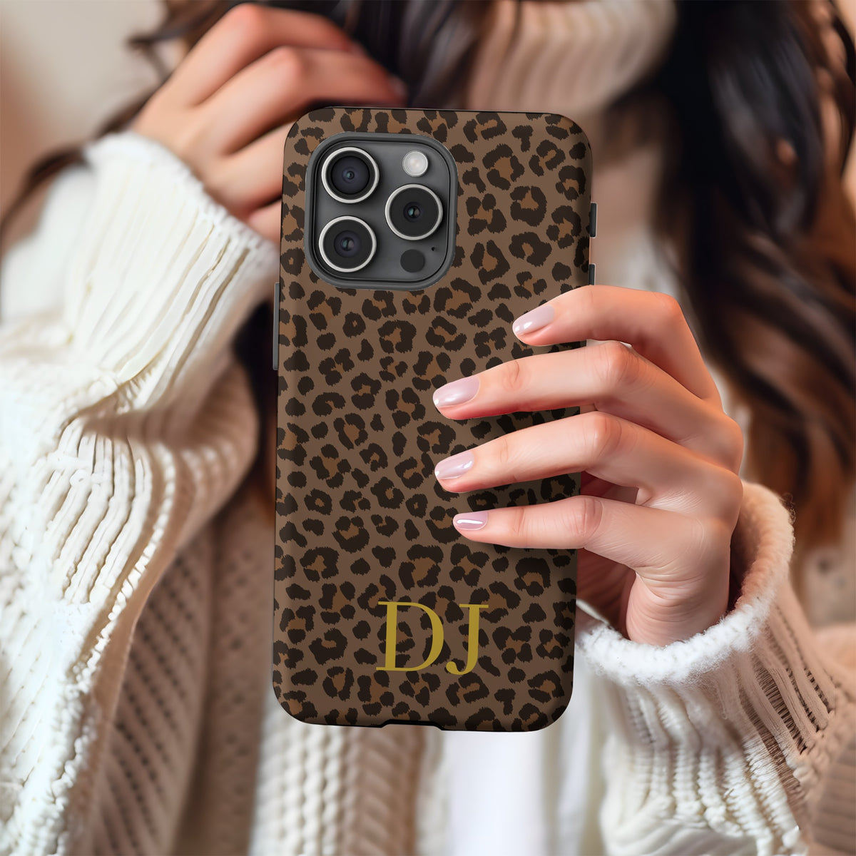 Brown leopard print tough phone case with gold initials held against a cream knit sweater