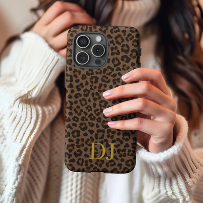 Brown leopard print tough phone case with gold initials held against a cream knit sweater
