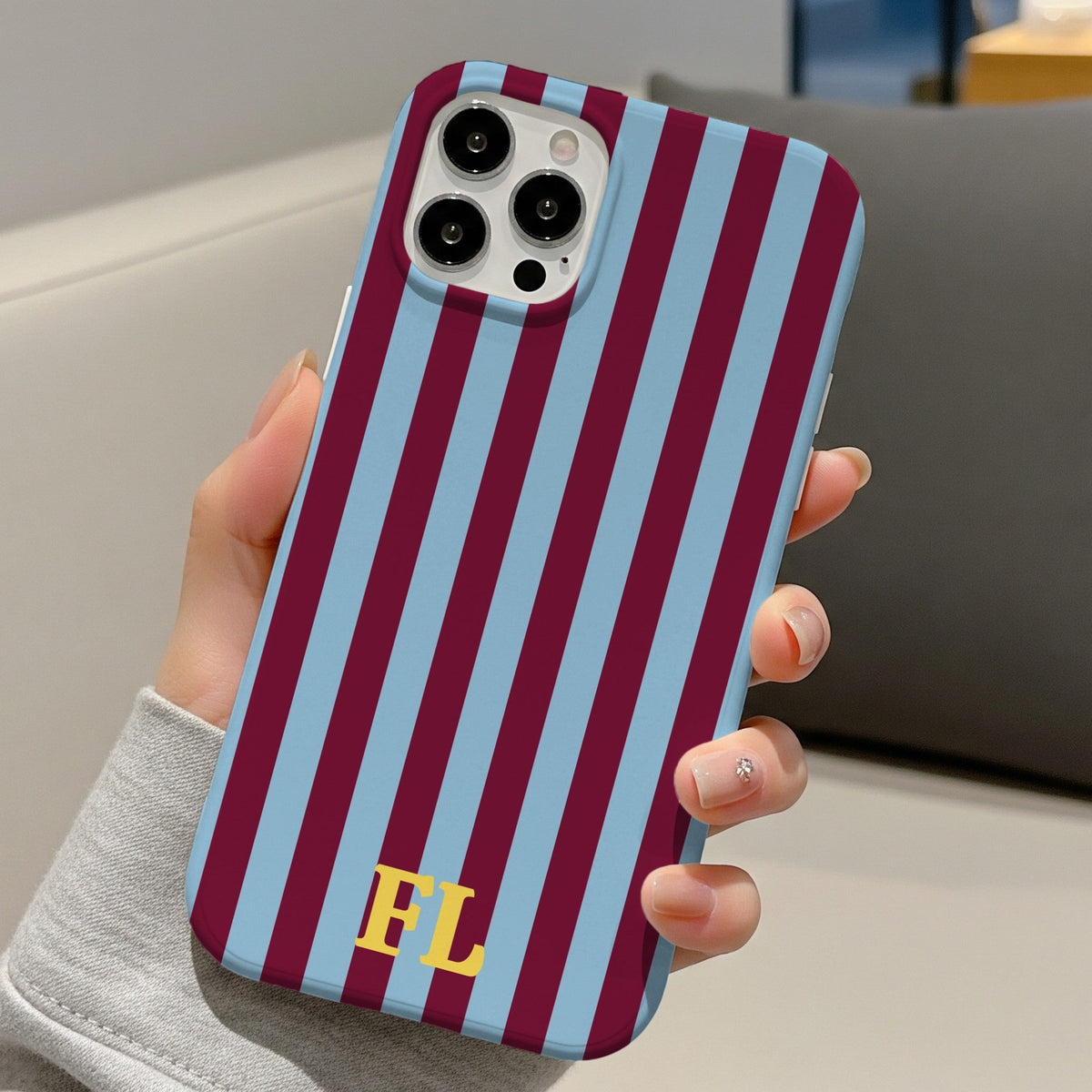 Burgundy cabana stripe phone case with initials, held in one hand at a desk