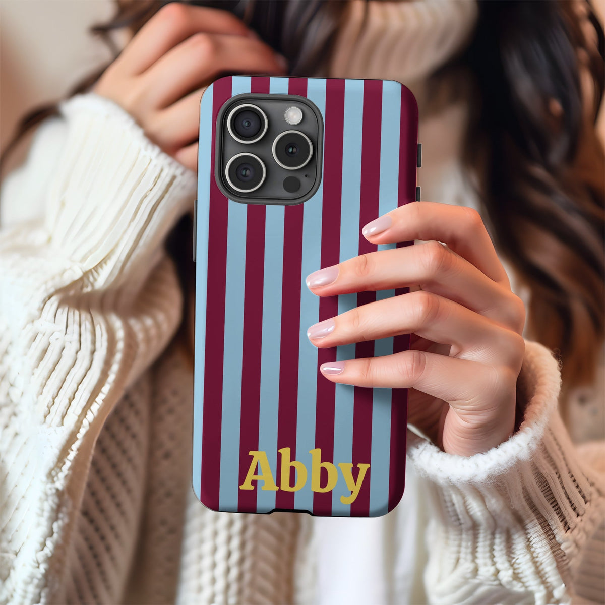 Burgundy cabana stripe phone case held in hand against a cream knit sweater