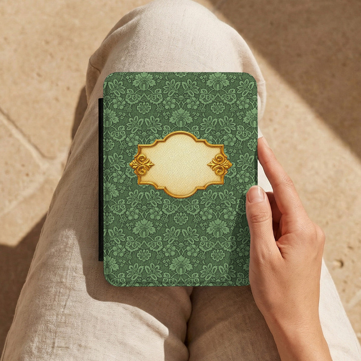 Hand holding the Emerald Damask Kindle case on a lap