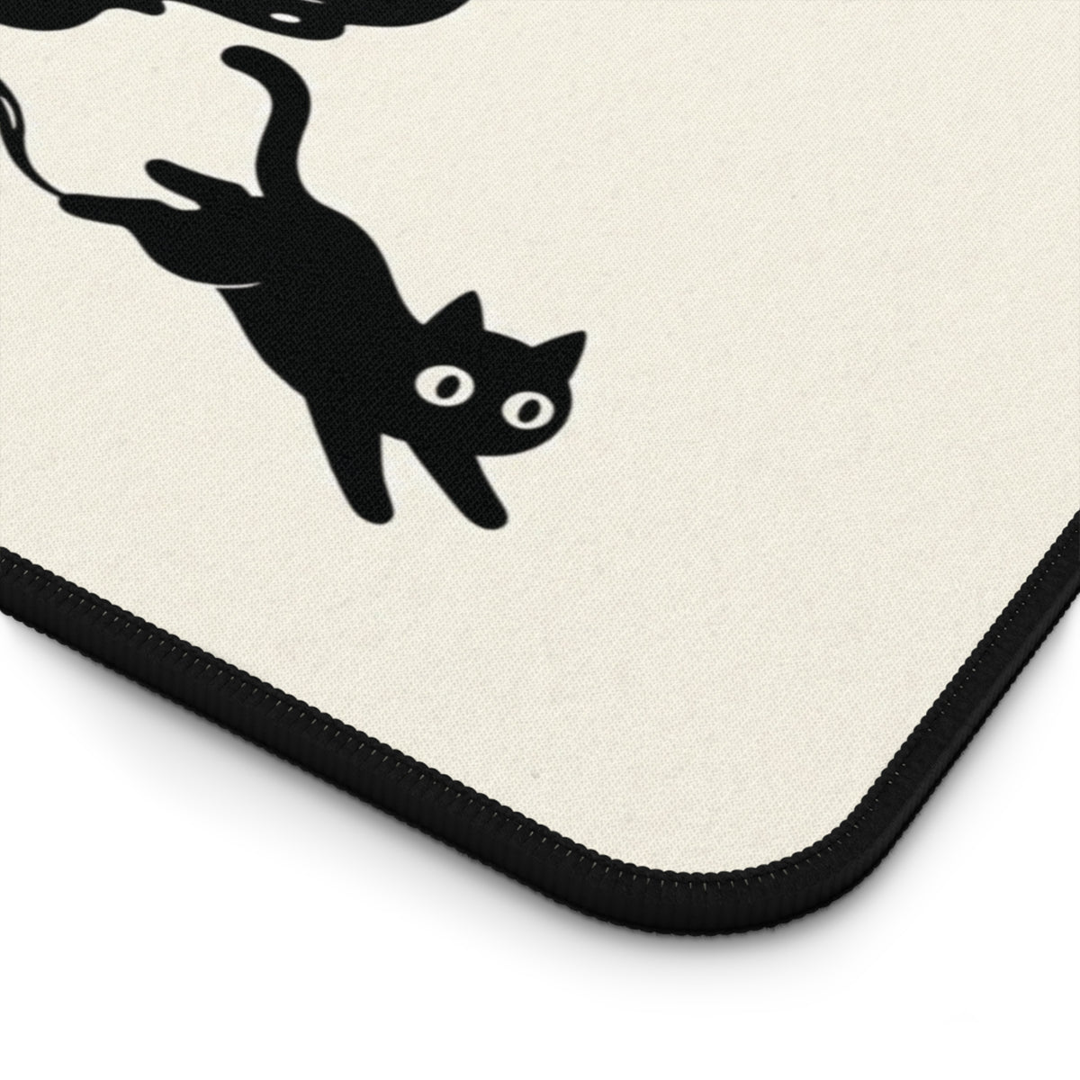 Close-up of the stitched edge and rounded corner of the Ink Spill Cats desk mat