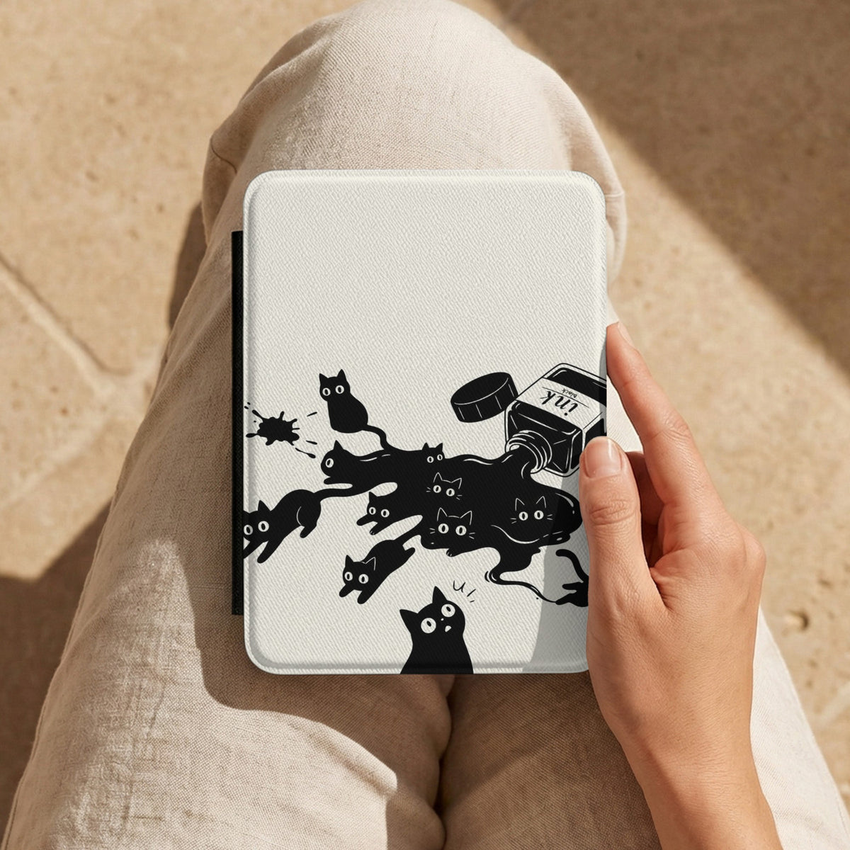 Ink Spill Cats Kindle case held on a lap while reading