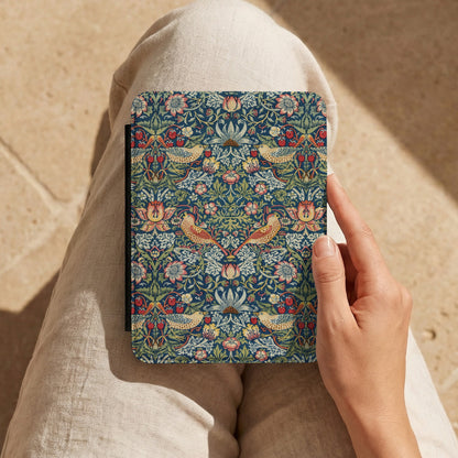 Hand holding a Morris Strawberry Thief Kindle case on a lap