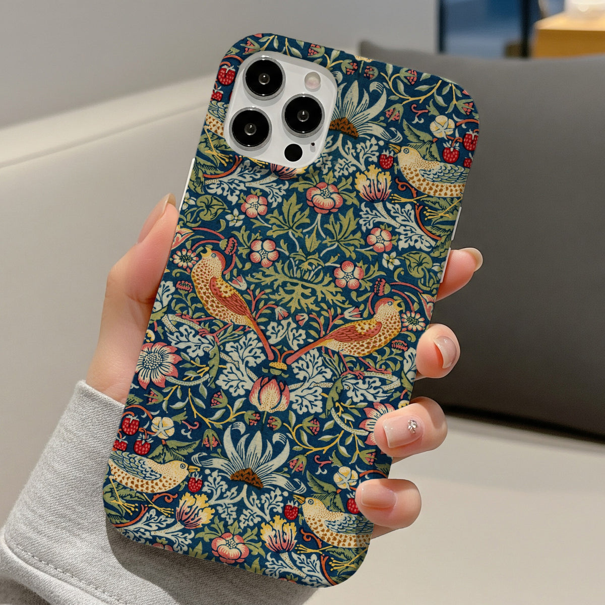 Morris Strawberry Thief tough phone case held in hand on a sofa