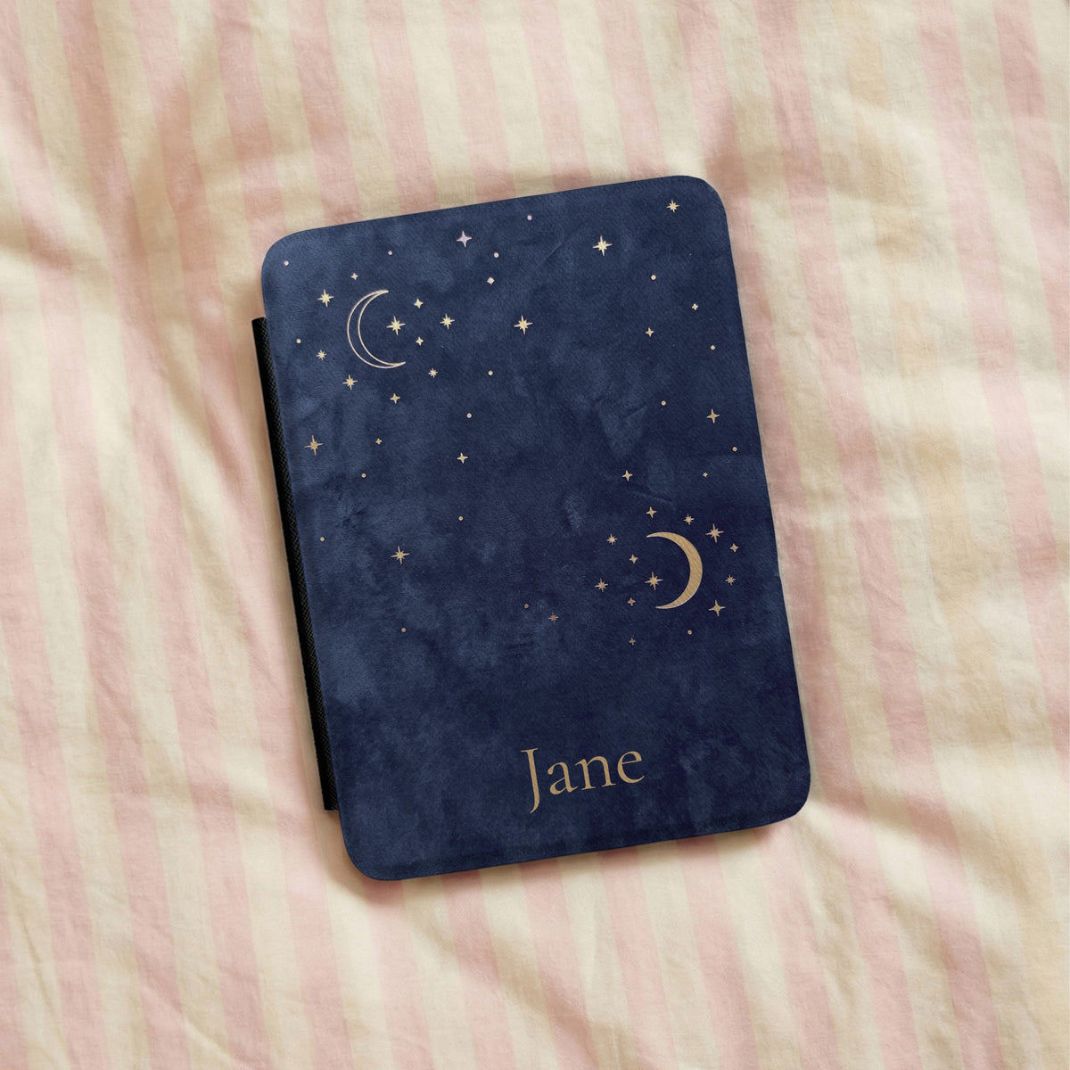 Navy Crescent Moon Kindle case with a name, lying on striped bedding