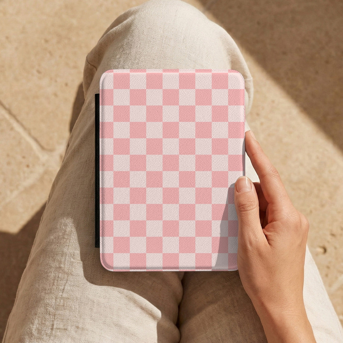 Pink Checkerboard Kindle case held on a lap while reading