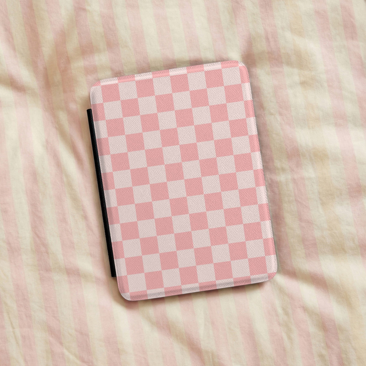 Pink Checkerboard Kindle case resting on striped bedding