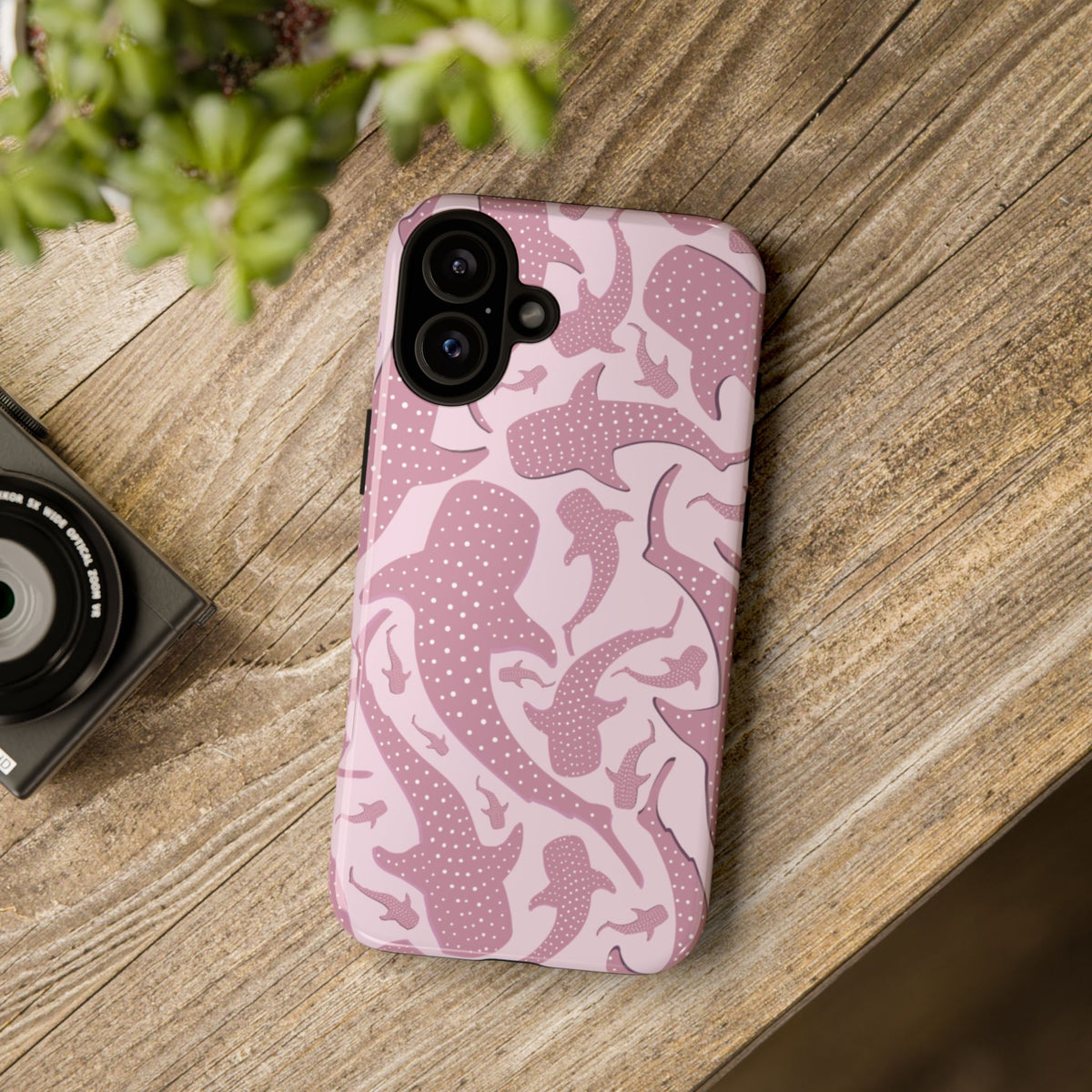 Pink Whale Shark phone case lying on a wooden table beside a camera