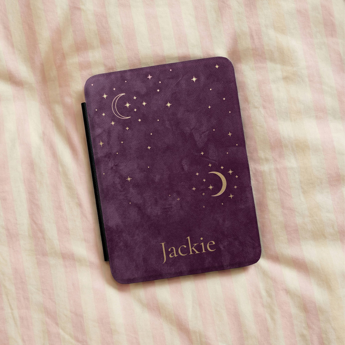 Plum Crescent Moon Kindle case with a name, lying on striped bedding