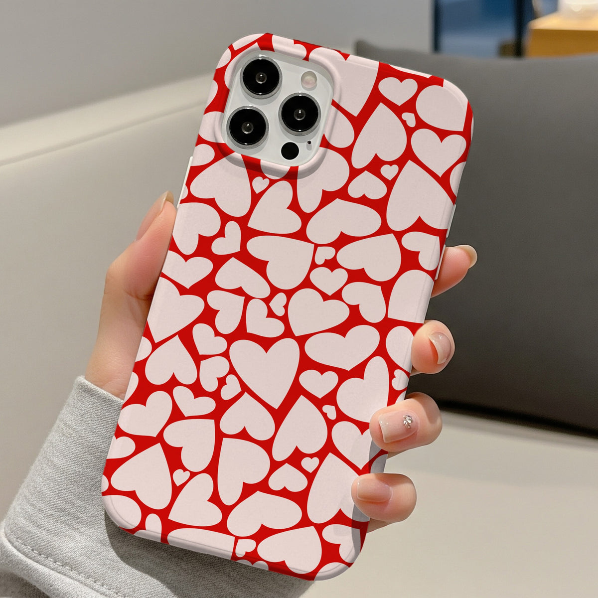 Red Hearts tough phone case held in one hand on a sofa
