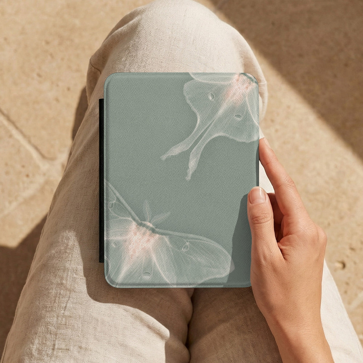 Sage Luna Moth Kindle case held on a lap in cream trousers