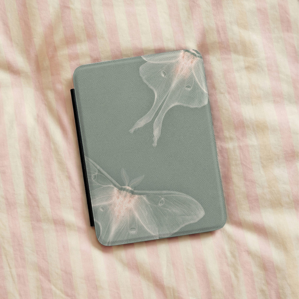 Sage Luna Moth Kindle case lying on striped bedding