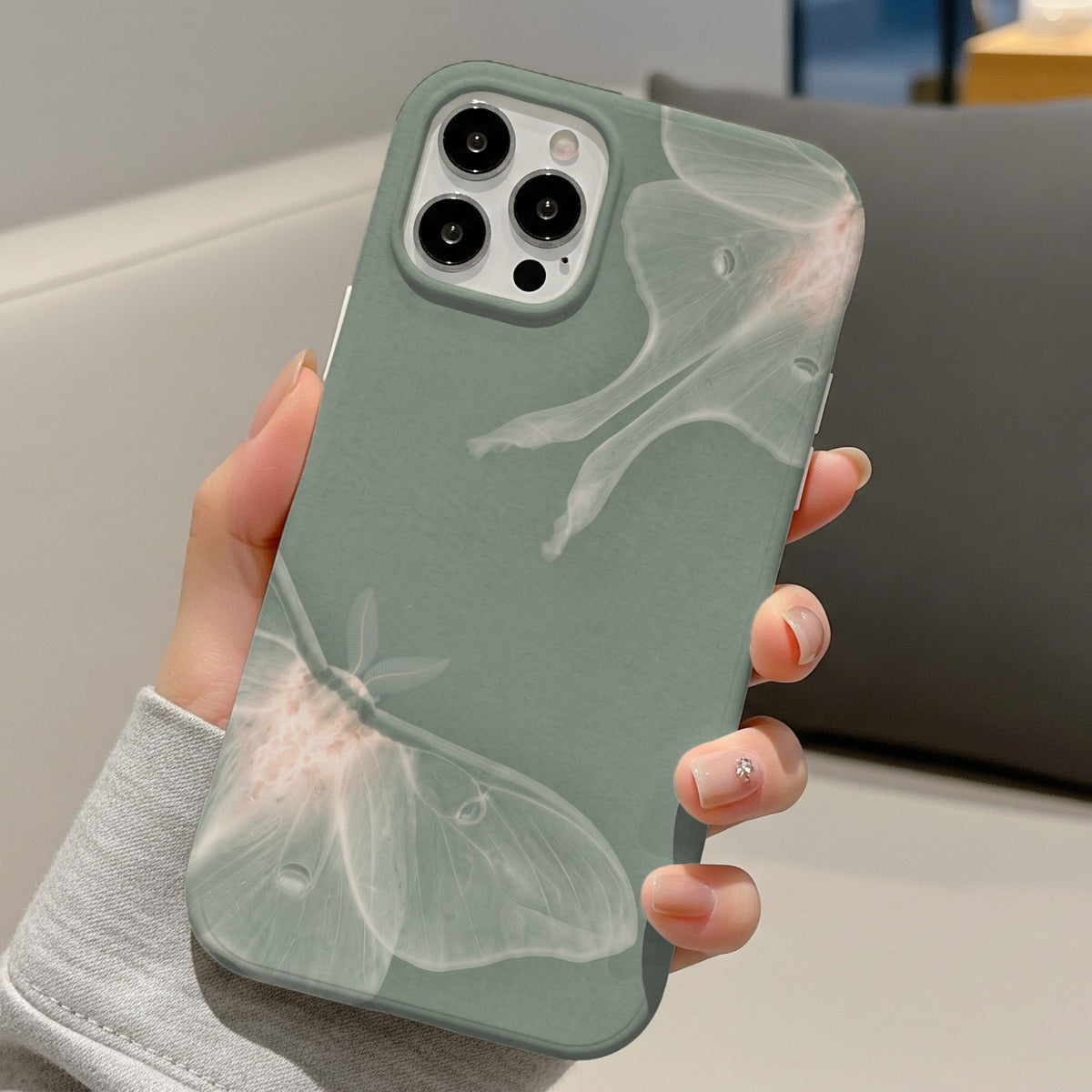 Sage Luna Moth tough phone case held in one hand on a sofa